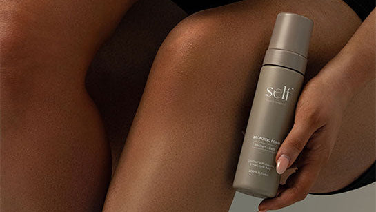 Two bottles of 'self' hair removal product held by a person with dark skin.