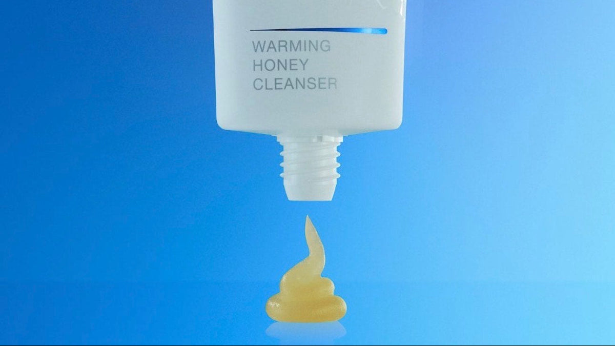 Tube of IS Clinical Warming Honey Cleanser with a small amount of cream on a blue background