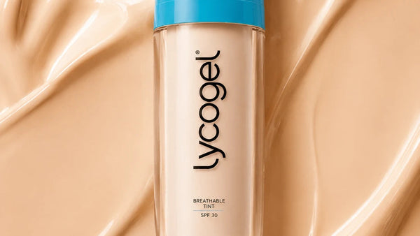 A bottle of Lycogel Breathable Tint SPF 25 foundation with a bright blue cap, centered on a background of smooth, swirled beige foundation cream.