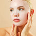 Woman applying a face mask with a beige background