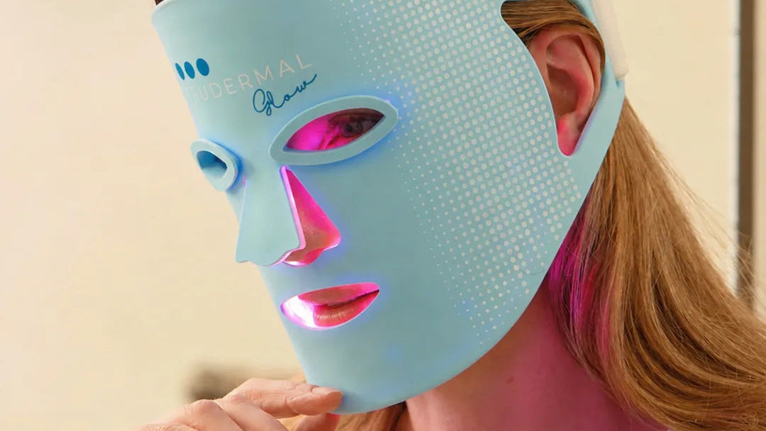 Woman wearing a blue LED face mask with visible branding on a beige background